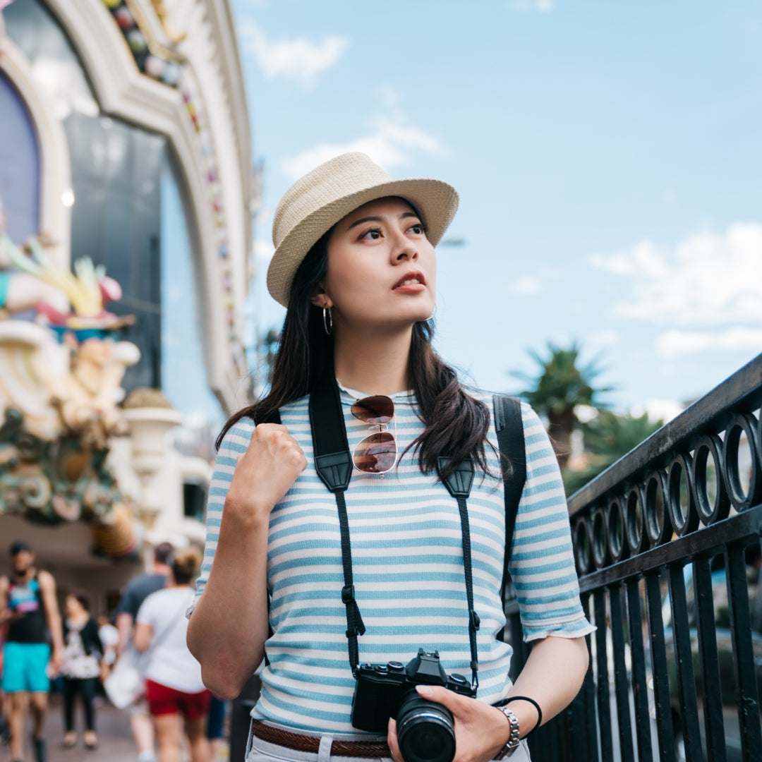 Woman in a striped shirt and hat with a camera, standing outdoors with a Ferris wheel in the background.