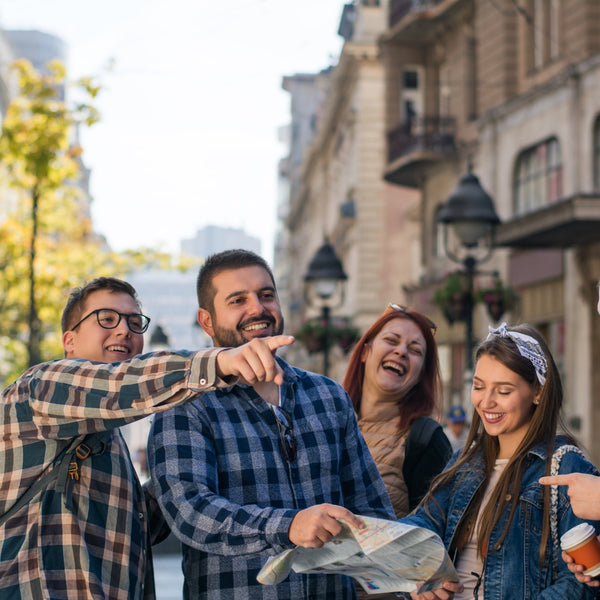 Group of four friends laughing and pointing at something on a city street.