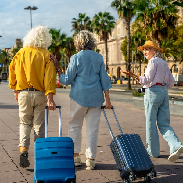 Three people with suitcases walking on a sunny day in an urban setting with palm trees.